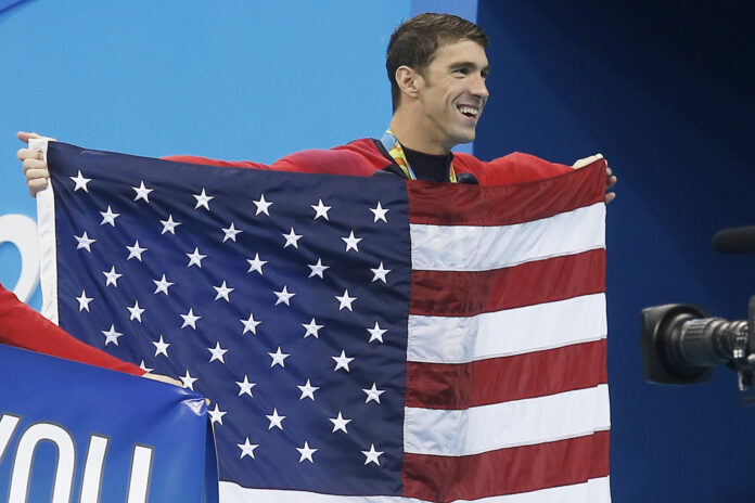 United States' Michael Phelps walks with his national flag during the medal ceremony for the men's 4 x 100-meter medley relay final during the swimming competitions at the 2016 Summer Olympics